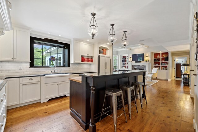 kitchen with white cabinetry, sink, a center island, light hardwood / wood-style flooring, and backsplash