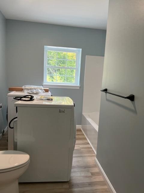 bathroom with hardwood / wood-style floors, toilet, a bath, and washer / clothes dryer