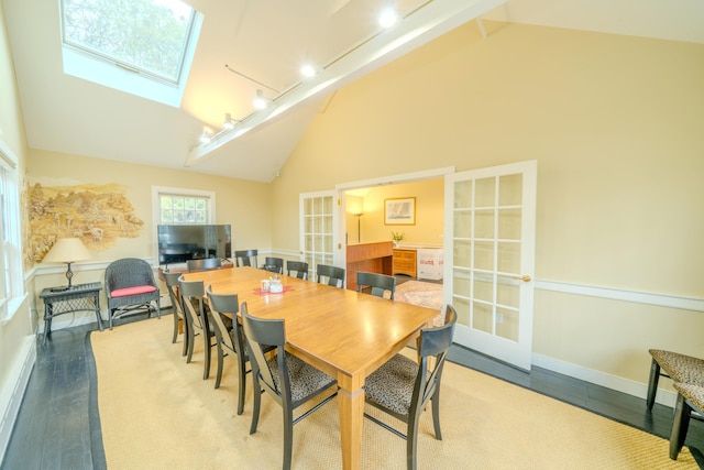 dining room featuring high vaulted ceiling, track lighting, french doors, a skylight, and light wood-type flooring