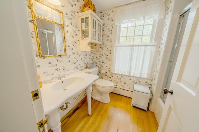 full bathroom featuring bath / shower combo with glass door, baseboard heating, sink, hardwood / wood-style flooring, and toilet