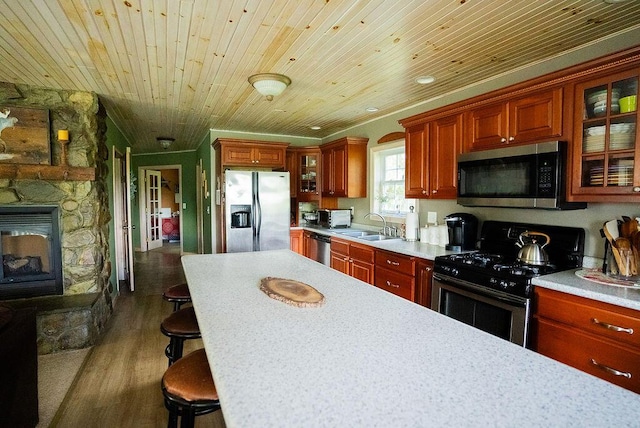 kitchen with a kitchen breakfast bar, stainless steel appliances, dark wood-type flooring, wooden ceiling, and a stone fireplace