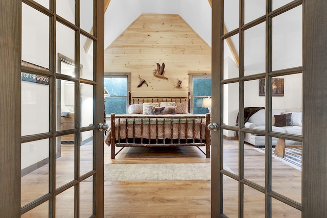 bedroom with high vaulted ceiling, wood-type flooring, french doors, and wooden walls