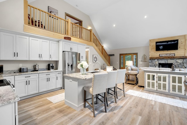 kitchen with sink, an island with sink, a kitchen breakfast bar, white cabinets, and light stone counters