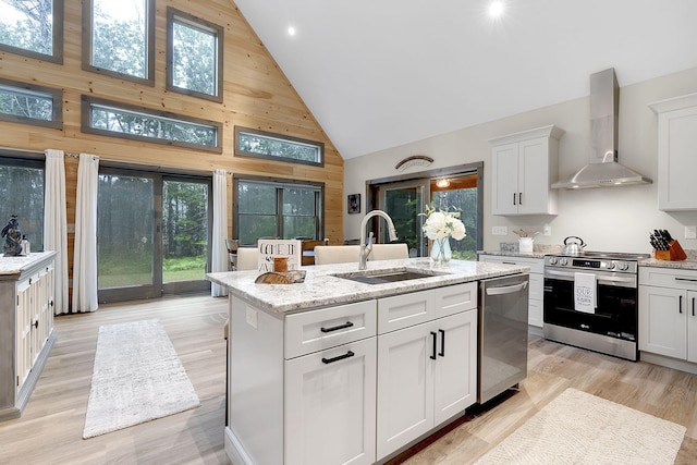 kitchen featuring appliances with stainless steel finishes, wall chimney exhaust hood, sink, high vaulted ceiling, and a center island with sink