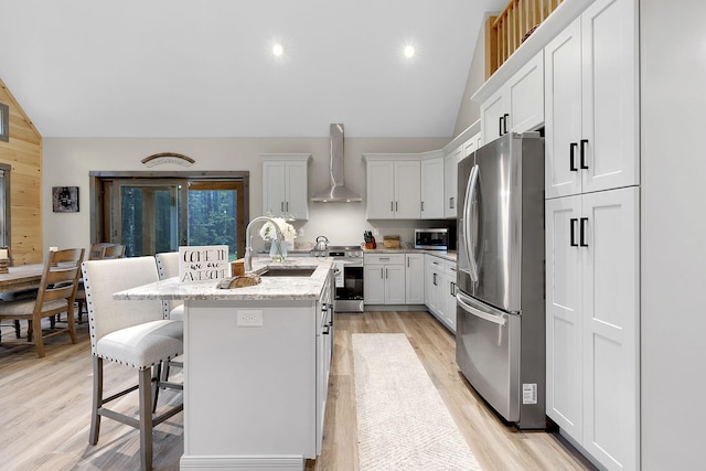 kitchen with a breakfast bar, white cabinetry, appliances with stainless steel finishes, an island with sink, and wall chimney exhaust hood