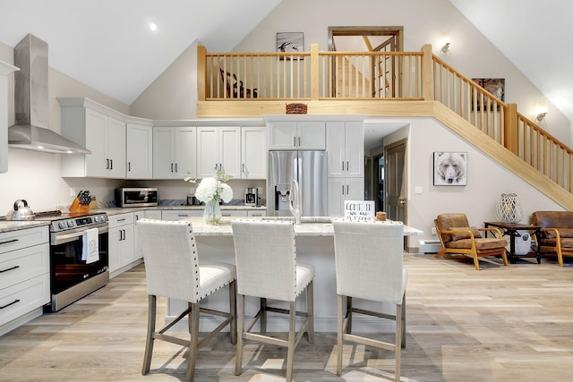 kitchen featuring white cabinets, wall chimney range hood, appliances with stainless steel finishes, and a kitchen island with sink