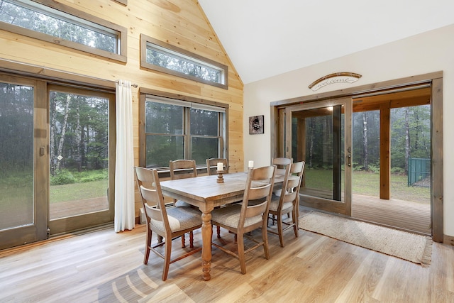 dining area featuring high vaulted ceiling, wood walls, and light hardwood / wood-style flooring