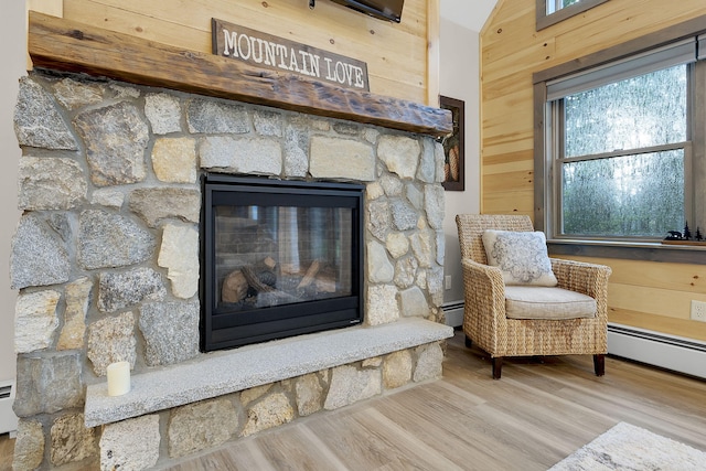 sitting room with baseboard heating, lofted ceiling, wood-type flooring, a fireplace, and wood walls