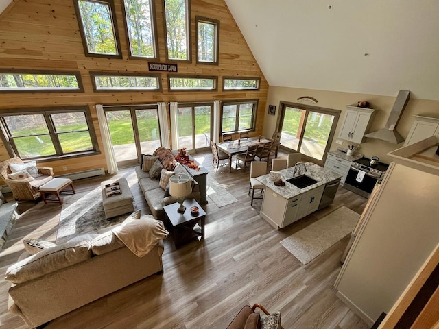 living room with a wealth of natural light, light hardwood / wood-style floors, wood walls, and high vaulted ceiling