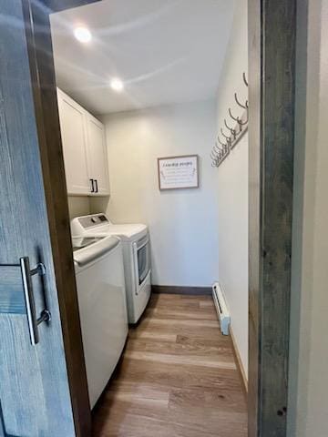 clothes washing area featuring light hardwood / wood-style floors, cabinets, a baseboard heating unit, and washing machine and dryer