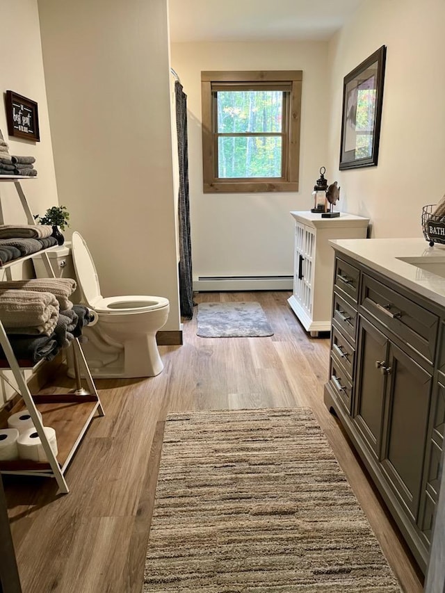 bathroom with hardwood / wood-style flooring, a baseboard heating unit, vanity, and toilet