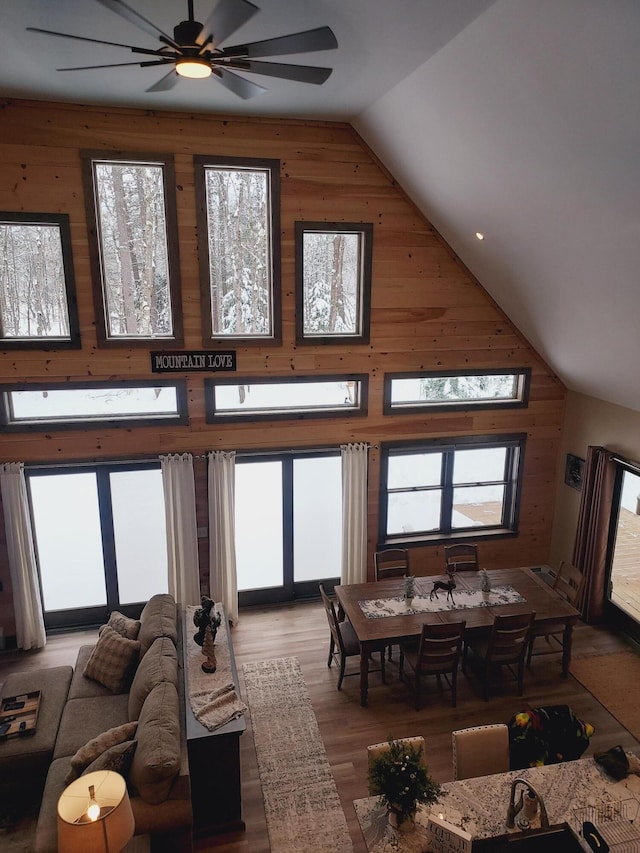 dining space with ceiling fan, wood-type flooring, high vaulted ceiling, and wood walls