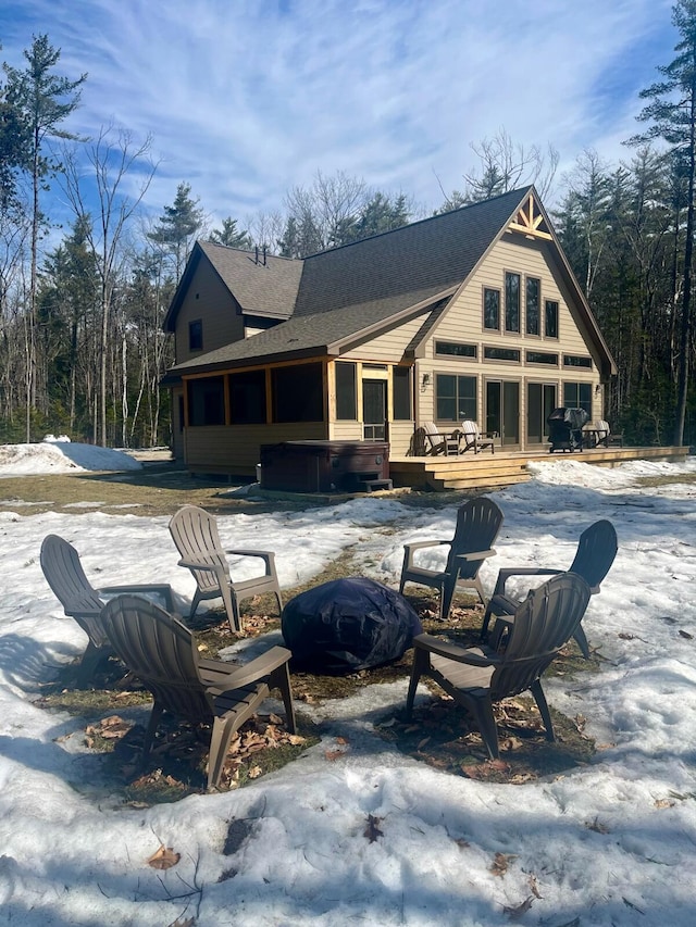 snow covered property featuring roof with shingles, a wooden deck, a sunroom, and an outdoor fire pit