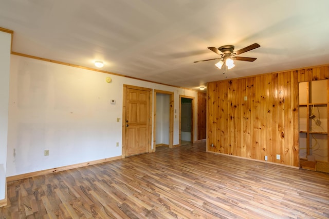 empty room with ornamental molding, light hardwood / wood-style flooring, ceiling fan, and wooden walls