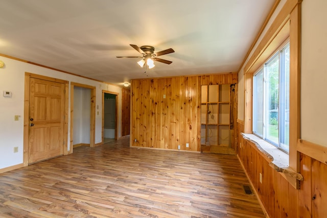 unfurnished room with hardwood / wood-style flooring, ceiling fan, a healthy amount of sunlight, and wood walls