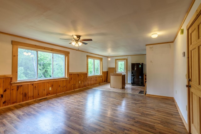 unfurnished living room with ceiling fan, dark hardwood / wood-style flooring, ornamental molding, and wooden walls