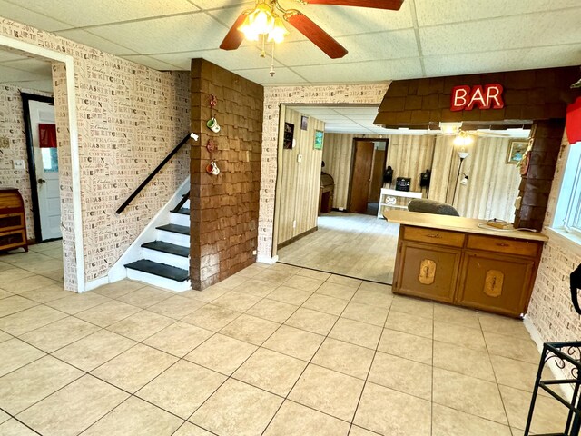 interior space with ceiling fan, a drop ceiling, and brick wall