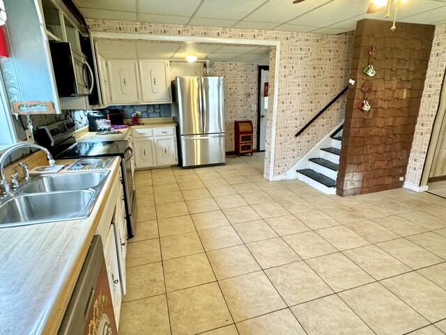 kitchen featuring brick wall, appliances with stainless steel finishes, sink, a drop ceiling, and light tile patterned floors