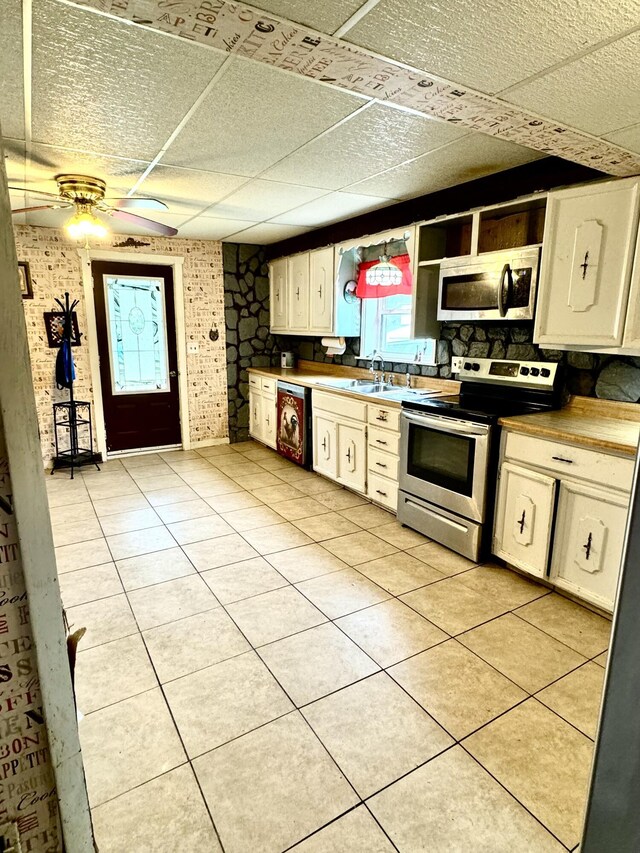 kitchen with light tile patterned floors, ceiling fan, stainless steel appliances, brick wall, and sink