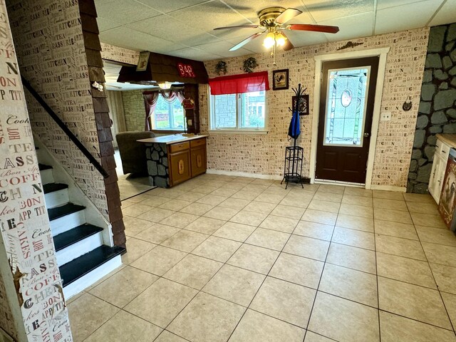 foyer entrance featuring ceiling fan, light tile patterned floors, a drop ceiling, and brick wall