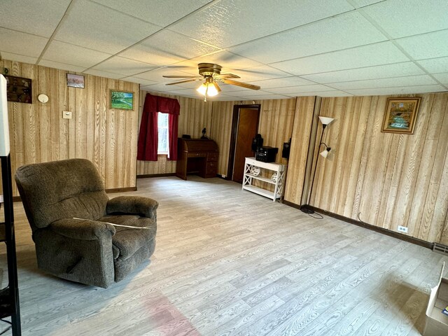 living room featuring wood walls, ceiling fan, wood-type flooring, and a drop ceiling