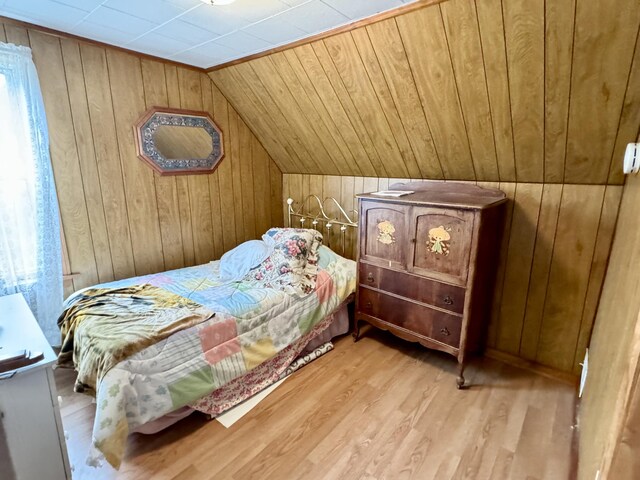 bedroom featuring vaulted ceiling, light wood-type flooring, and wooden walls