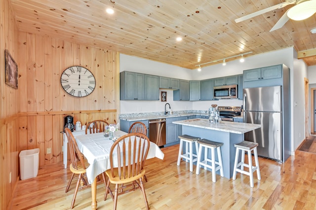 kitchen featuring appliances with stainless steel finishes, light stone counters, light hardwood / wood-style floors, and wooden ceiling