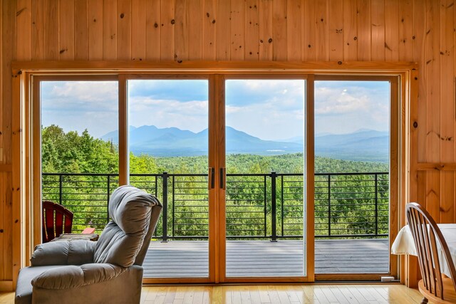 doorway to outside with light hardwood / wood-style floors, a mountain view, wooden walls, and a healthy amount of sunlight