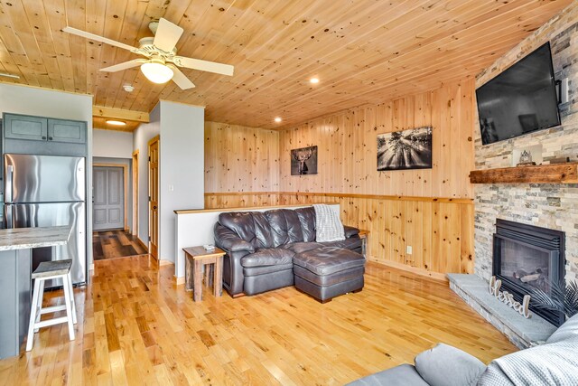 living room featuring ceiling fan, light wood-type flooring, wood ceiling, wood walls, and a fireplace