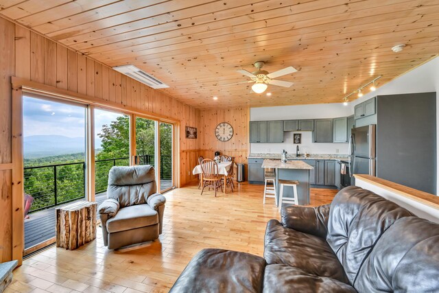 living room with rail lighting, light wood-type flooring, wooden walls, ceiling fan, and wooden ceiling