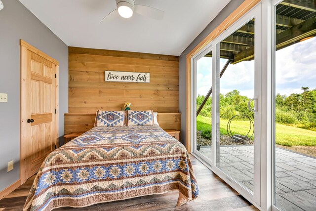 bedroom with ceiling fan, access to outside, hardwood / wood-style flooring, and wood walls