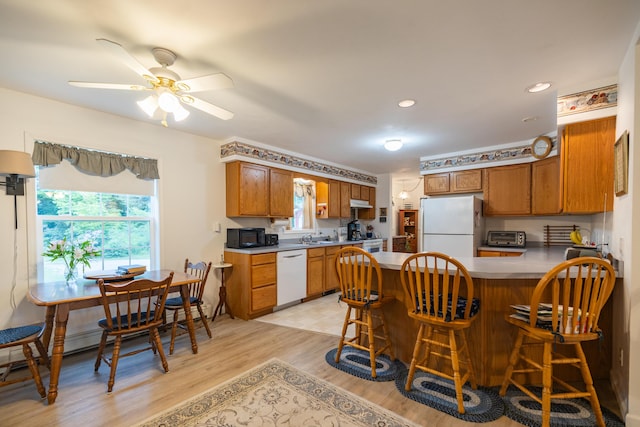 kitchen with white appliances, a kitchen breakfast bar, ceiling fan, light wood-type flooring, and kitchen peninsula