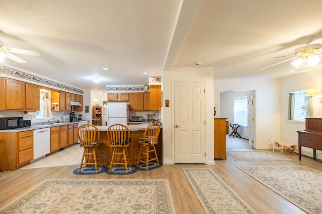 kitchen with light wood-type flooring, white appliances, ceiling fan, sink, and a breakfast bar area