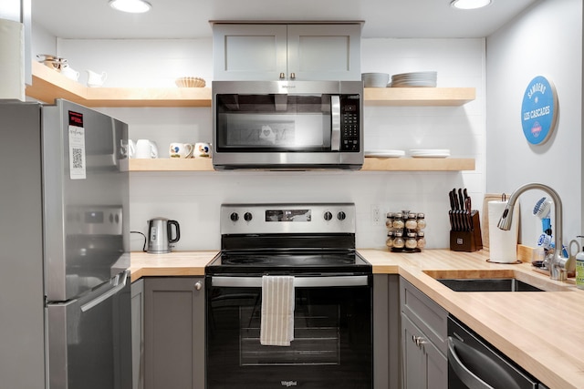 kitchen with stainless steel appliances, sink, backsplash, gray cabinets, and butcher block countertops