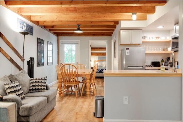 kitchen with sink, beamed ceiling, light wood-type flooring, stainless steel appliances, and white cabinets