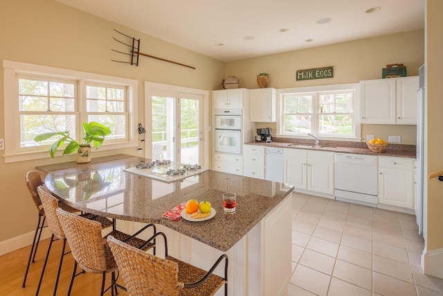 kitchen with a breakfast bar, a healthy amount of sunlight, white appliances, and white cabinetry