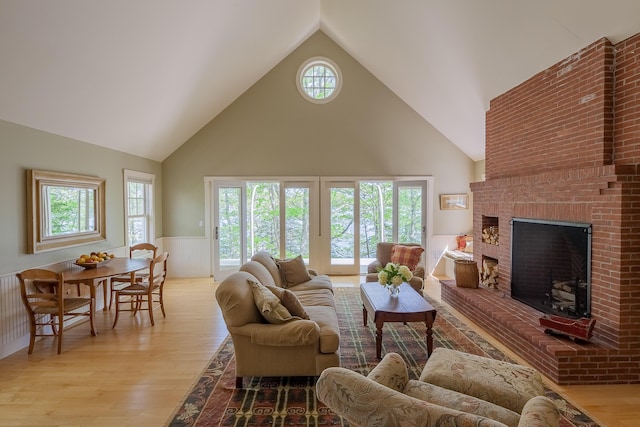 living room with high vaulted ceiling, light hardwood / wood-style floors, and a brick fireplace