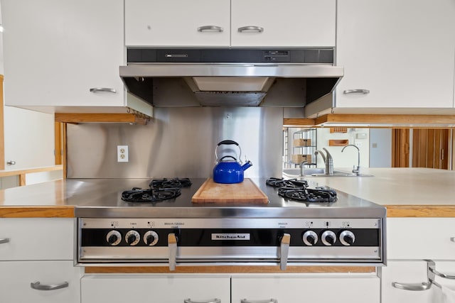 kitchen featuring white cabinets, stainless steel gas stovetop, exhaust hood, light countertops, and a sink