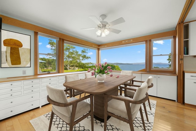dining room featuring light wood-type flooring, a healthy amount of sunlight, ceiling fan, and a water view