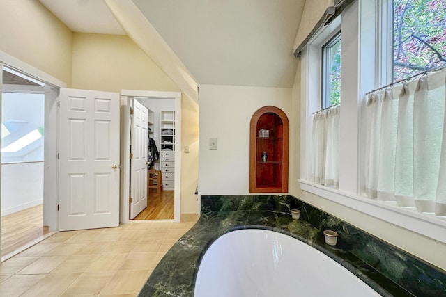 bathroom with hardwood / wood-style floors, a tub, and vaulted ceiling