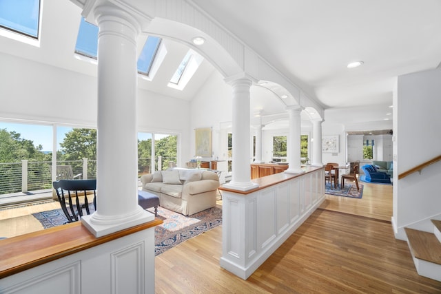 living room with light hardwood / wood-style floors, high vaulted ceiling, a skylight, and decorative columns