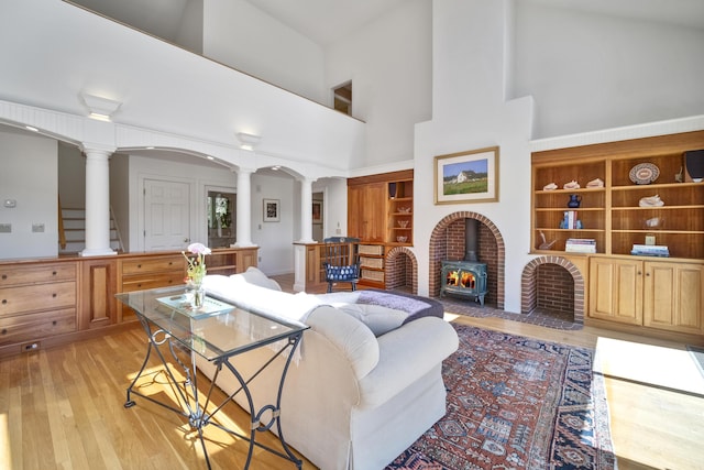 living room featuring a towering ceiling, light hardwood / wood-style floors, a wood stove, and decorative columns