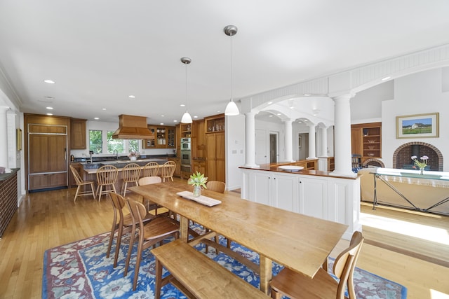 dining area featuring ornate columns, sink, and light hardwood / wood-style flooring