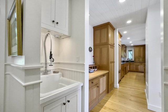 kitchen with sink, white cabinets, wooden ceiling, and light wood-type flooring