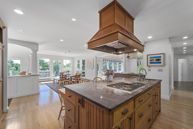 kitchen featuring stainless steel gas stovetop, a center island, ceiling fan, light wood-type flooring, and decorative columns