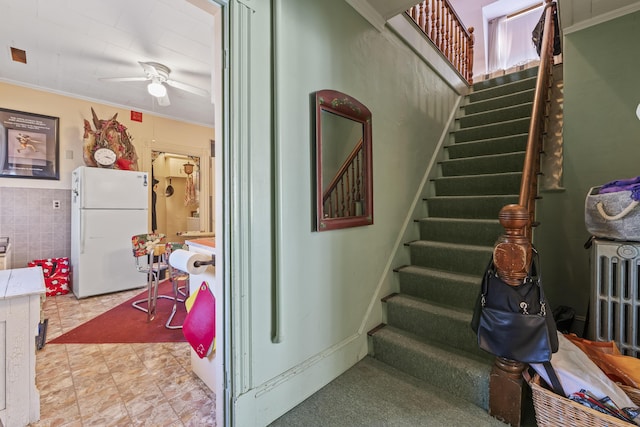 stairway with ceiling fan, tile walls, and ornamental molding