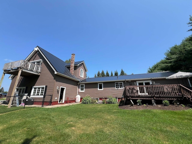 rear view of house with a deck, metal roof, fence, a yard, and a chimney