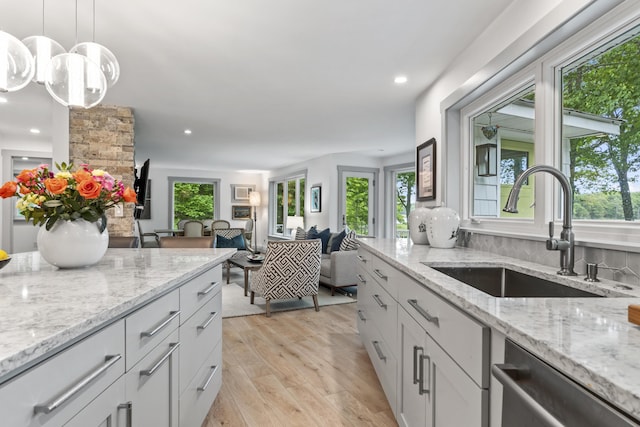 kitchen featuring sink, light hardwood / wood-style floors, light stone countertops, decorative light fixtures, and stainless steel dishwasher