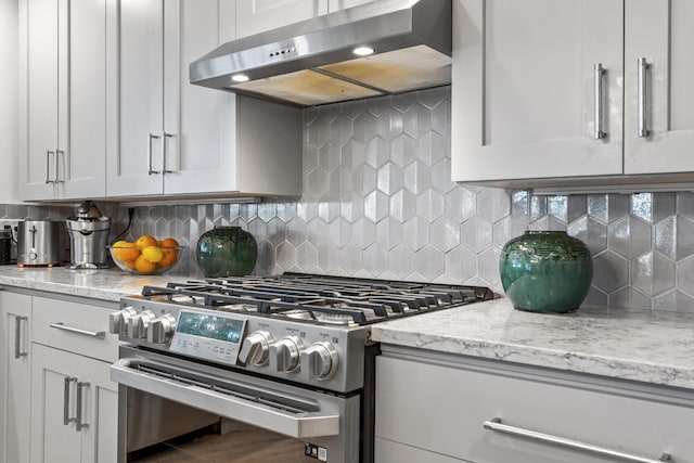 kitchen featuring stainless steel gas stove, wall chimney range hood, light stone counters, and white cabinets