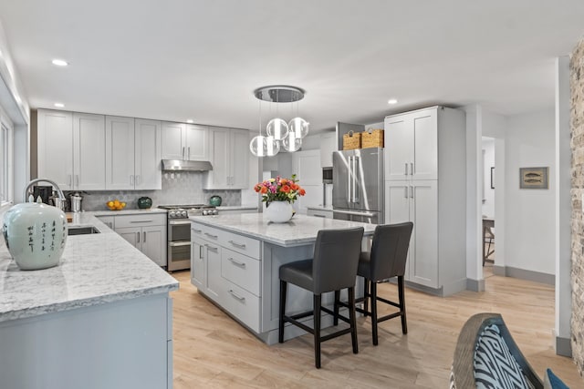 kitchen with light hardwood / wood-style flooring, gray cabinets, backsplash, stainless steel appliances, and decorative light fixtures